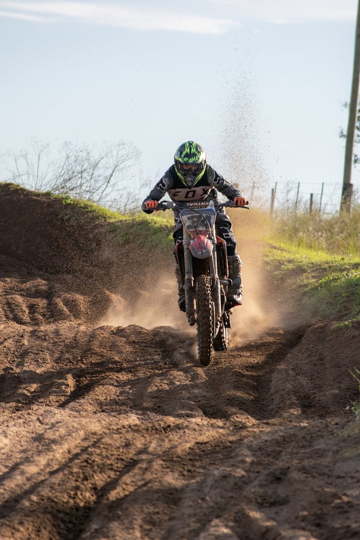 A Person Wearing a Black and White Racing Suit Riding a Motorcycle on Soil